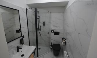 A modern bathroom with a glass shower and maritime tiles. There are sinks, a toilet, and a minimalist design.