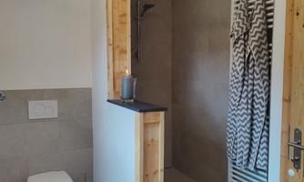 A modern bathroom with a shower and a toilet. The walls are light and there is a towel radiator.