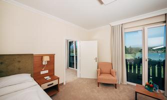 A cozy room with a double bed, an armchair, and a table. Large windows offer a view of the landscape outside.