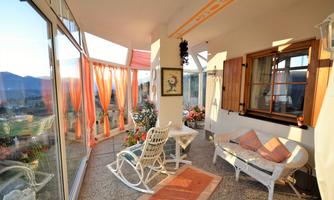 A cozy porch with large windows and a view of the mountains. There is a table, chairs, and colorful curtains that create a relaxed atmosphere.