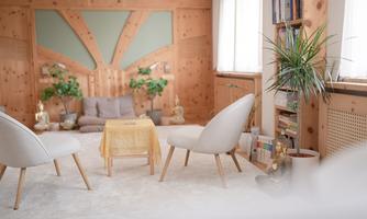 A cozy room with wooden paneling, two comfortable chairs, and a small coffee table in the middle of the room. Plants and bookshelves create an inviting atmosphere.