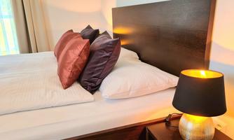 A cozy bedroom with a large bed and colorful pillows. Next to the bed, there is a stylish lamp that emits warm light.