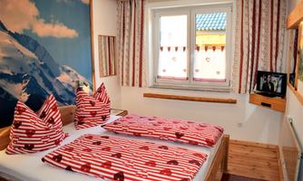 A cozy bedroom with a double bed and red-white striped bedding. The room has large windows with an outside view and an alpine wall decoration.
