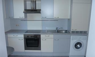 A modern kitchen with light cabinets and a stove. The sink and a washing machine are also available.