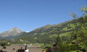 A picturesque mountain landscape with green hills and a clear blue sky. In the foreground, beautiful flowers and traditional cottages can be seen.