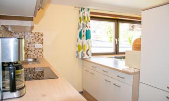 A modern kitchen with bright wood and colorful curtains. The window lets in plenty of daylight.
