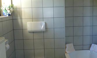A modern bathroom with a bathtub and a toilet. The walls are brightly tiled, and there is a blue bath mat.