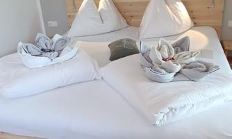 A cozy bedroom with a wooden bed and neatly folded towels. The walls are painted in soft colors, and a picture hangs on the wall.
