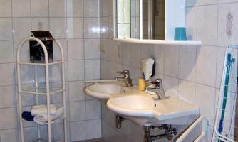 A simple bathroom with two sinks and a mirror. There is a towel rack and a laundry basket in the corner.