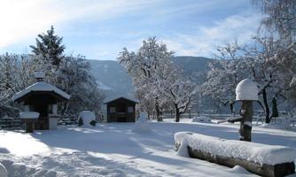 A snowy landscape with a calm atmosphere. Trees and buildings are covered in snow and the sky is blue.