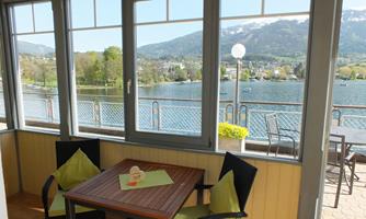 A cozy balcony overlooking a lake and the surrounding mountains. There are two chairs and a small plant decoration at the table.