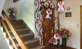 An inviting hallway with a wooden staircase and an ornate railing. Traditional dolls and colorful flower arrangements hang on the wall.