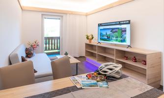 A bright, cozy apartment with a sofa and a large TV. On the table are a pair of sunglasses, a map, and a bike helmet.