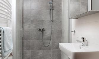 A modern bathroom with a shower and a sink. The walls are in neutral gray tones, and there is a large mirror.