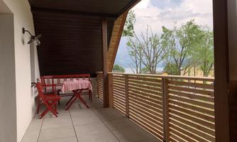 A balcony with a red table and chairs. In the background, there are trees and a clear sky.