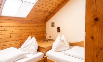 A cozy room with wooden paneling and two beds. There is a table lamp and a small window that provides natural light.