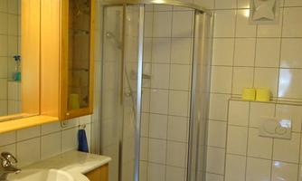A modern bathroom with a shower and a sink. The walls are covered with white tiles and there is a wooden cabinet with a mirror.