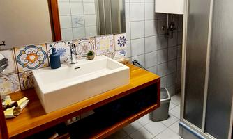 A modern bathroom with a shower and a sink on a wooden base. The walls are decorated with light tiles and colorful accents.