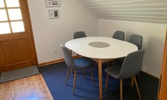 A modernly furnished dining area with a round table and six chairs. The room has a cozy ambiance with wooden flooring and a bright atmosphere.