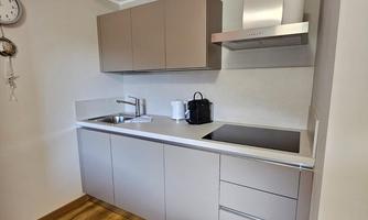 A modern kitchen with bright cabinets and a cooktop. The floor is made of wood and there is a clock on the wall.