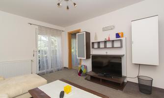 A modern living room with a cozy sofa and a television. The room has large windows that let in plenty of daylight.
