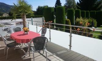 A beautiful balcony with a round table and chairs. In the background, well-maintained hedges and colorful flowers can be seen.