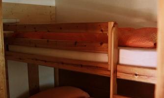 A simple room with a wooden bunk bed. The mattresses are covered with orange sheets and pillows.