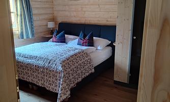A modern bedroom with wooden interior. The bed is cozy and decorated with colorful cushions.