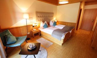 A cozy room with a double bed and modern furniture. There is an armchair and a table, as well as warm light for an inviting atmosphere.