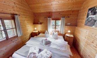 A cozy wooden bedroom with two beds and white bedding. The windows let in plenty of daylight and create an inviting atmosphere.