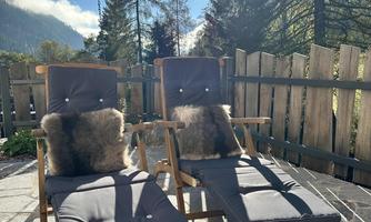 Two cozy lounge chairs are on a terrace overlooking trees and mountains. The sun shines brightly in the clear sky.