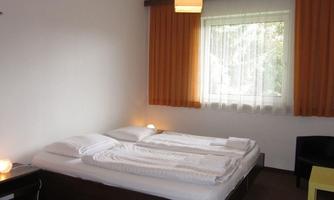 A simple room with two beds and a large window. The orange curtain creates a warm atmosphere.