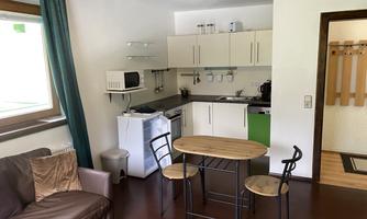 A small, modern kitchen with a dining area and a cozy sofa. Plenty of daylight streams through the windows.