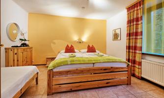 A cozy bedroom with a large double bed and two decorative pillows. The walls are painted in warm shades of yellow, and there is a pleasant atmosphere created by the natural light.