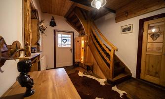 An inviting hallway with a wooden staircase and rustic decor. The floor is covered with a carpet in animal fur look.
