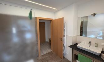 A modern bathroom with a glass shower cabin and a sink. The walls are bright and the decor is simple and functional.