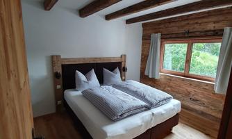 A cozy bedroom with a double bed and rustic wooden details. Large windows provide bright light and a pleasant atmosphere.