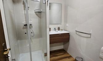 A modern bathroom with a glass shower and a vanity. The floor is tiled with a wood look, and the walls are kept bright.