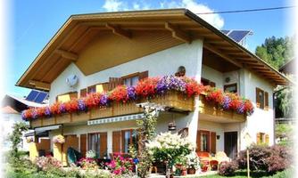 A charming house with colorful flower boxes and a large balcony. The surroundings are green and inviting.