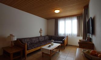 A cozy living room with a sofa and a table.  
Large windows let in plenty of light, and there is a lamp as well as a television.