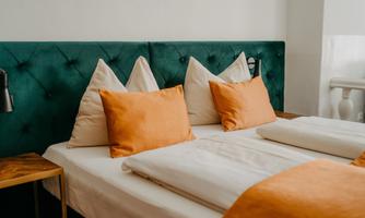 A bright and modern bedroom with a green velvet headboard and cozy cushions in neutral and orange tones. There are two nightstands with lamps and a calm, inviting atmosphere.