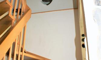 A wooden staircase leads upwards. A painting and a decorative flower vase hang on the wall.
