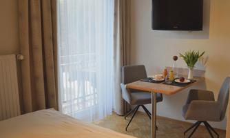 A cozy hotel room with a bed and a small table. On the table, there are drinks and fruit, and there is a television on the wall.