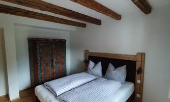 A cozy bedroom with a large bed and wooden details. The room has bright walls and impressive wooden ceiling beams.