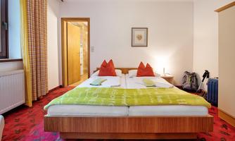 A cozy bedroom with a double bed and red pillows. The room is bright and friendly, with a carpet and a window.