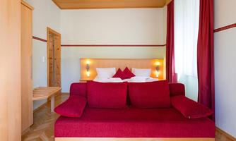 A cozy room with a red sofa and a double bed. Large windows let in plenty of daylight.