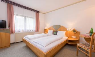 A bright room with a double bed and wooden furniture. There is a television, nightstands, and a table with chairs.