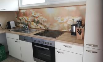 A modern kitchen with a wooden workspace and a beautiful backsplash design featuring flowers. The kitchen utensils are neatly stored, and the appliances are well placed.
