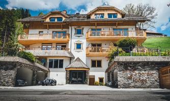 A modern chalet with wooden embellishments and balconies. Surrounded by green hills and under a blue sky.