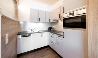 A modern kitchen with light cabinets and an elegant design. The amenities include an oven and a sink.